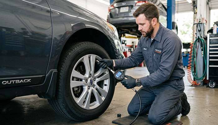Auto mechanic in gray uniform checking tire pressure with a gage on a car wheel.