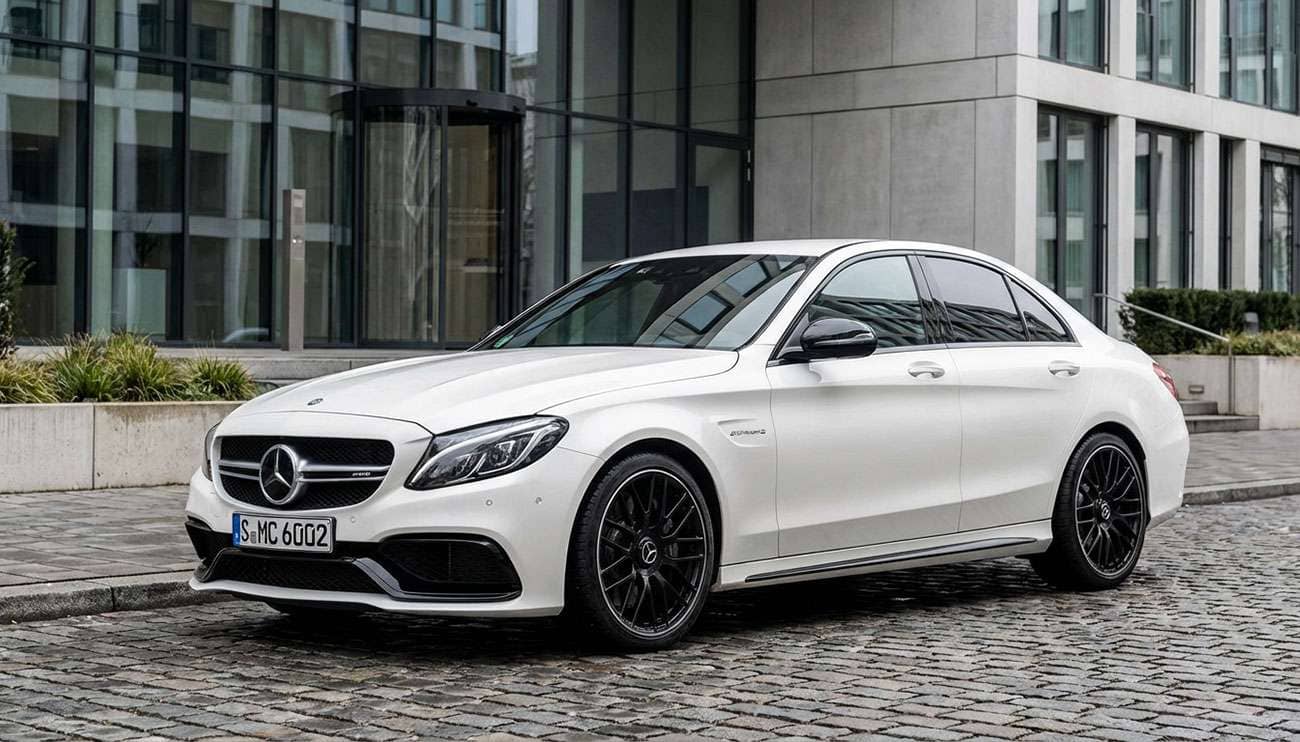 White Mercedes-Benz C-Class AMG sedan with black AMG wheels parked on cobblestone near a modern building