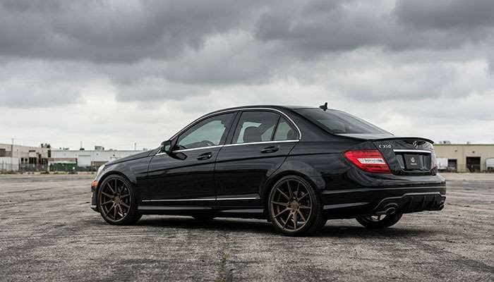 Black Mercedes-Benz C350 W204 with aftermarket wheels parked in an empty lot under a cloudy sky