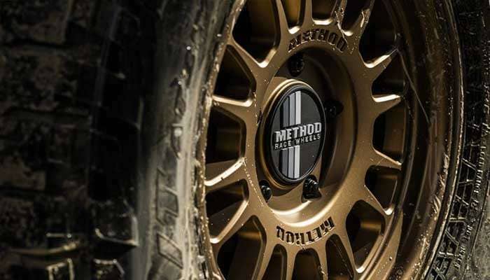 Close-up of a bronze Method Race Wheels off-road wheel with rugged tire tread and mud splatters