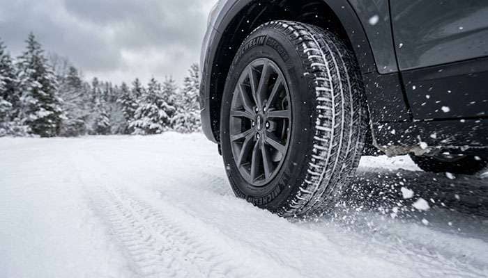 Close-up of a Michelin Defender tire on a snowy road demonstrating winter traction capabilities.