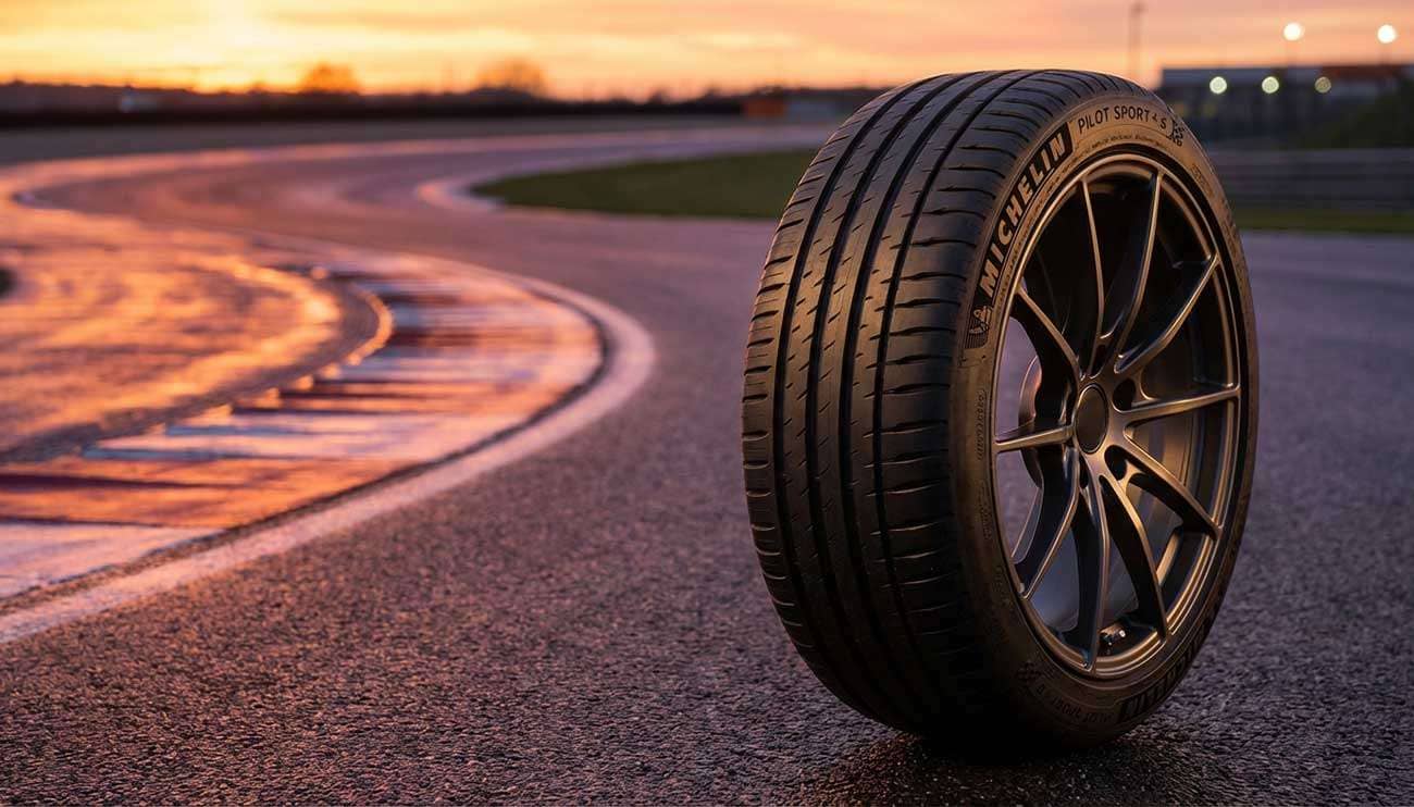 Close-up of a Michelin Pilot Sport 4 S tire on a sports car parked by a wet racetrack at sunset