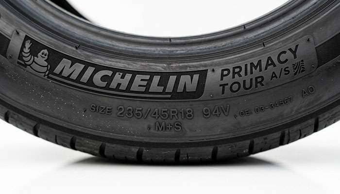 Close up of a Michelin Primacy Tour A/S tire sidewall showing the size marking and original equipment automaker code