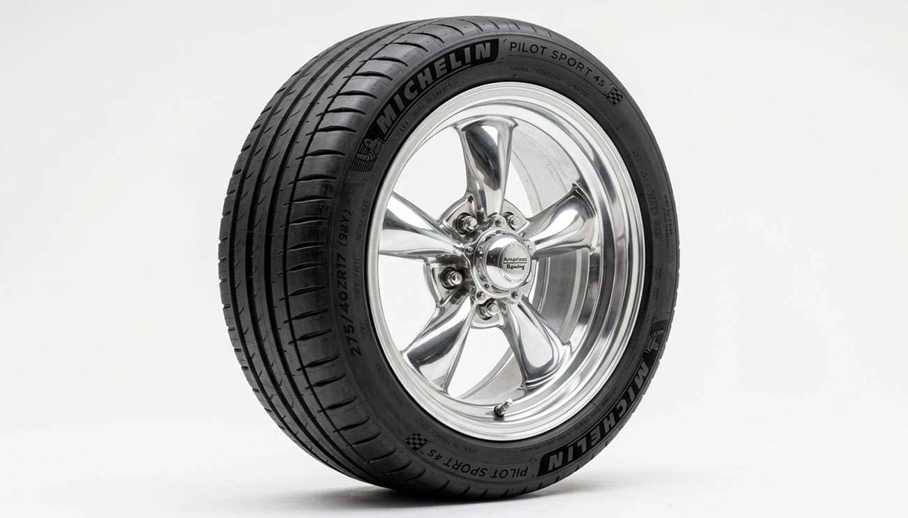 Modern radial tire mounted on a classic American muscle car wheel in a sunlit shop driveway