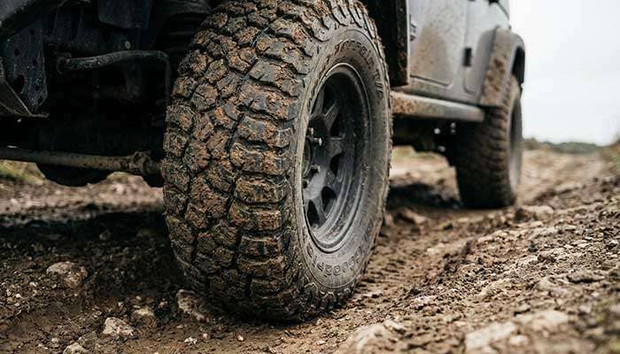 Close-up of a muddy all-terrain tire on a vehicle driving on a rugged off-road path