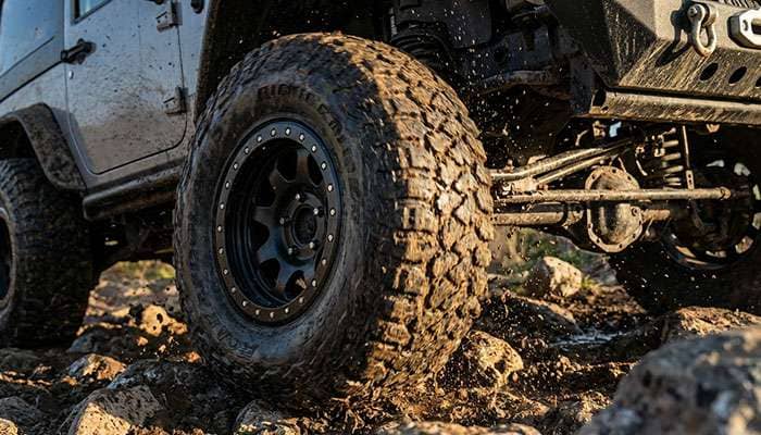 Close-up of a muddy off-road tire with a black beadlock rim mounted on a vehicle climbing a rocky terrain