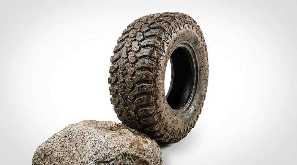 Close-up of a muddy off-road tire gripping a large rock during rock-crawling terrain driving
