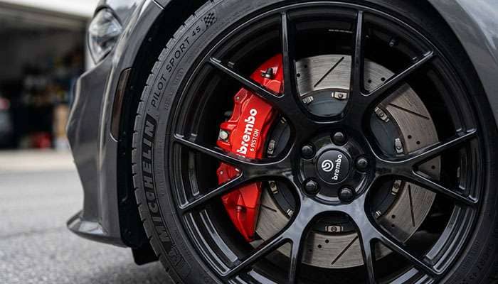 Close-up of a large red six-piston brake caliper and 16-inch rotor behind a 20-inch black performance wheel on a modern muscle sedan