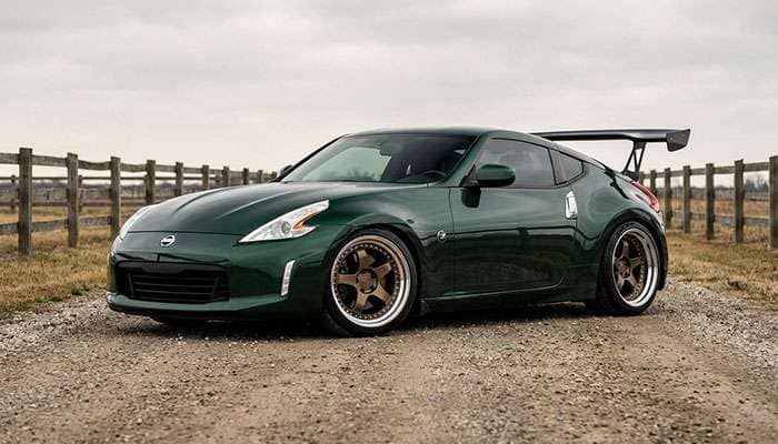 Green Nissan 370z with custom three-piece wheels and large rear wing parked on a rural road with wooden fences