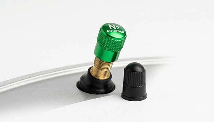 Green nitrogen valve cap on a tire valve stem next to a standard black air valve cap on a clean white studio backdrop