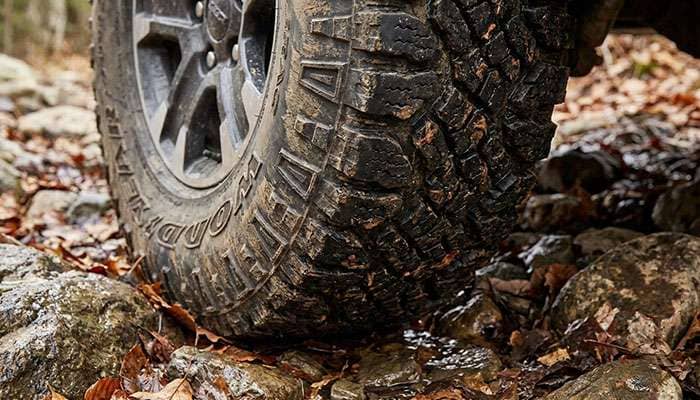 Close-up of a Nitto Recon Grappler all-terrain tire gripping rocky, leaf-covered ground