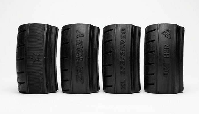 Close-up comparison of several tire sidewalls showing different manufacturer approval markings molded into the rubber