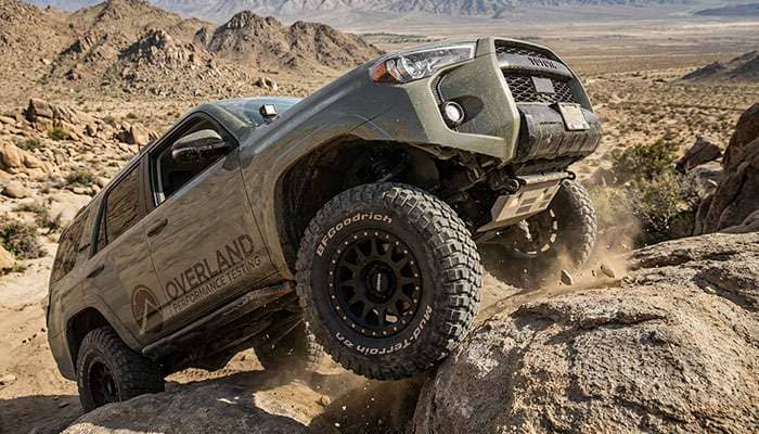 Off-road vehicle with aftermarket wheels navigating rocky terrain during performance testing