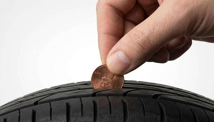 Hand holding a penny inserted into tire tread to check tread depth using the penny test.