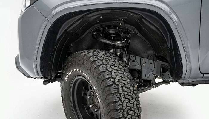 Front wheel well of a midsize pickup truck showing the fender liner, pinch weld seam, and body mount bracket behind the tire