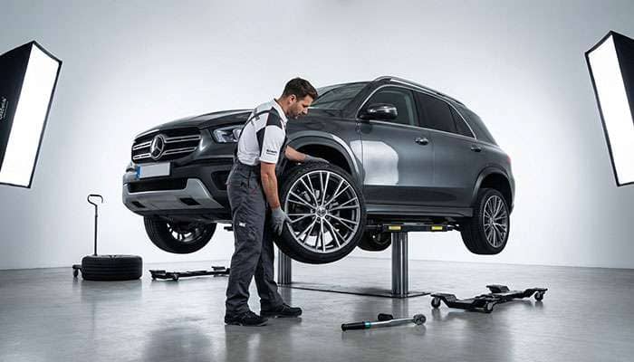 Professional mechanic installing a large plus-size alloy wheel onto a vehicle on a lift in a modern service bay