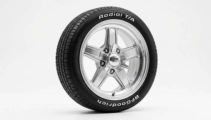 Polished classic five-spoke aluminum muscle car wheel on a white studio backdrop