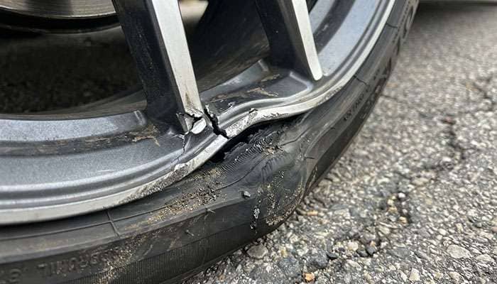 Close-up of damaged wheel rim from pothole impact showing bent metal and tire damage