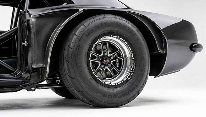 Tubbed rear wheel well of a pro street car showing the widened sheet metal needed to clear a wide rear drag tire on a clean white studio backdrop