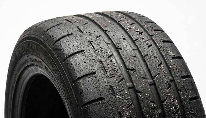Close-up of a heat-cycled R-compound track tire surface showing graining and wear after track use on a clean white studio backdrop