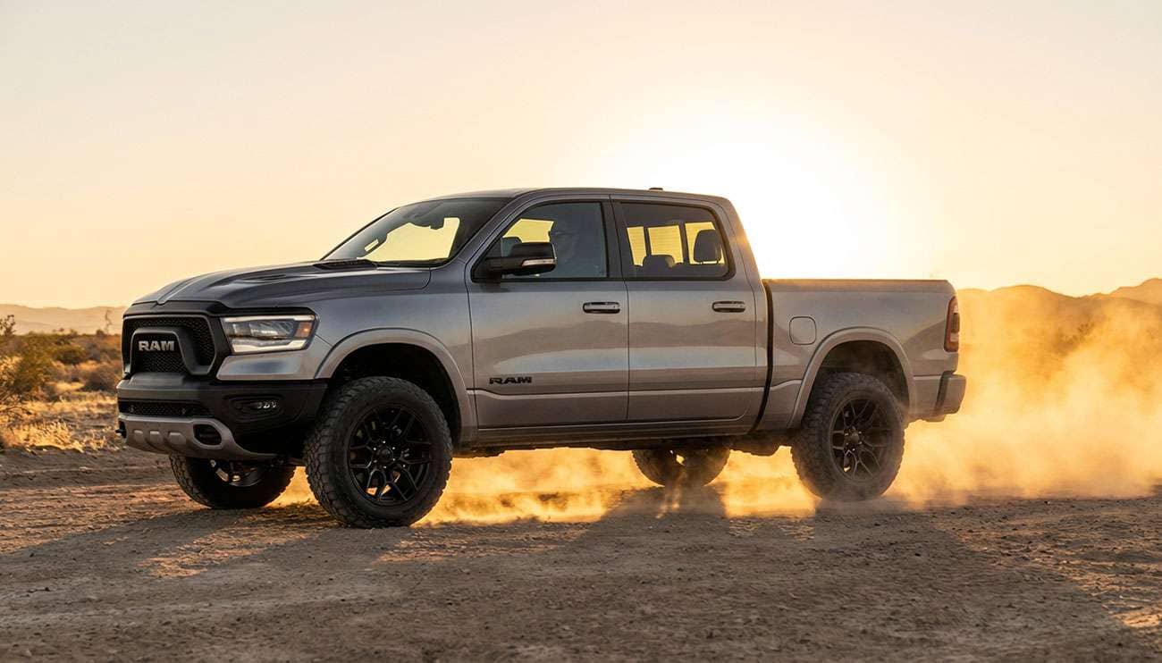 Close-up of a Ram 1500 pickup truck with aftermarket black alloy wheels on a dirt road at sunset