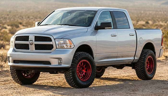 Silver Dodge Ram 1500 with custom red rims and off-road tires parked outside a building with Element Wheels signage