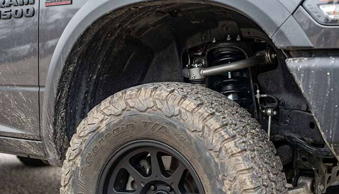 Close-up of a 35-inch all-terrain tire at full steering lock next to the upper control arm on a leveled Ram 1500