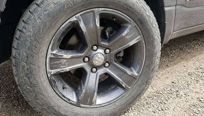 Close-up of a scratched and damaged cladded Ram 1500 wheel rim with a worn tire mounted