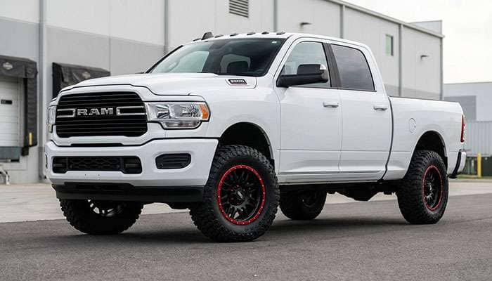 White current-gen RAM 2500 HD pickup truck with custom black and red wheels and off-road tires parked on pavement