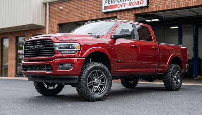Red third-generation RAM 2500 truck with large off-road wheels and tires parked on asphalt near a shop