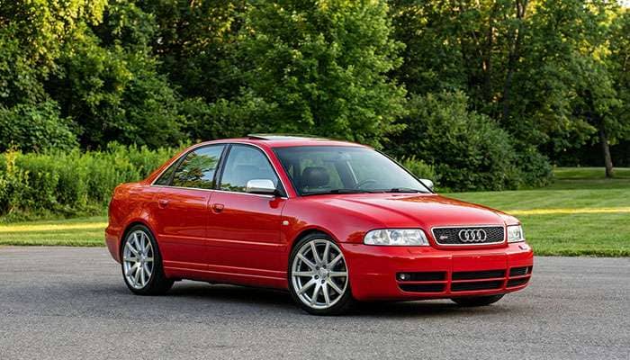 Red 2001 B5 Audi S4 sedan with silver rims parked on asphalt with green trees and grass in background