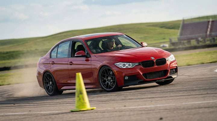Red BMW sedan with black wheels navigating a driving course marked by a yellow cone outdoors