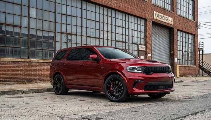 Red Dodge Durango equipped with Avant Garde AG M652 gloss black wheels parked in front of large industrial windows.