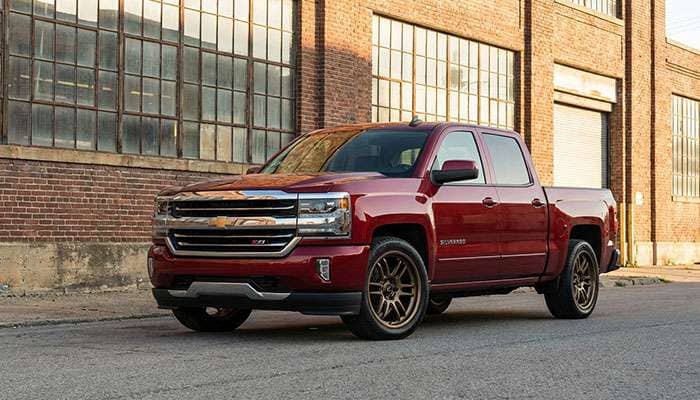 Red Chevrolet Silverado with Cosmis Racing wheels parked in front of a building in sunlight