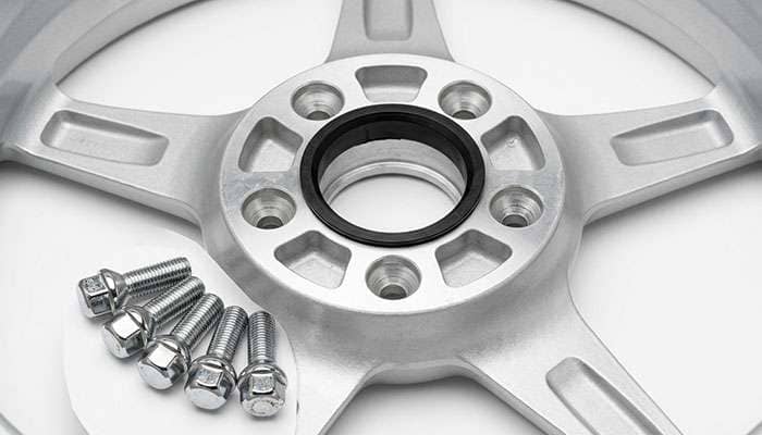 Aluminum replica wheel center showing the hub bore, a hub-centric ring, and conical lug seats next to ball-seat lug bolts