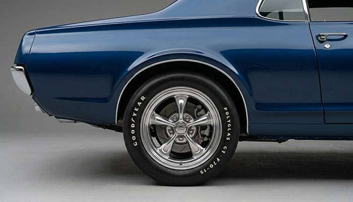 Fully restored and polished vintage cast aluminum wheel mounted on a classic American muscle car showing mirror finish and period-correct styling