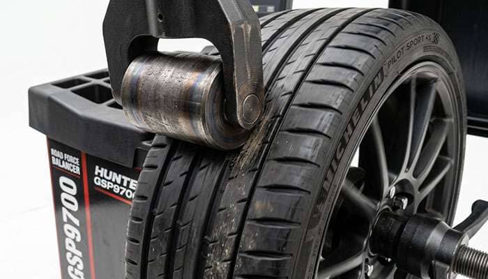 Close-up of a road force balancer load roller pressing against a spinning tire tread