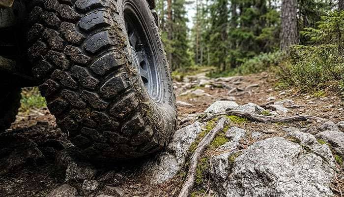 Close-up of a rugged off-road tire gripping rocky terrain in a forested trail setting