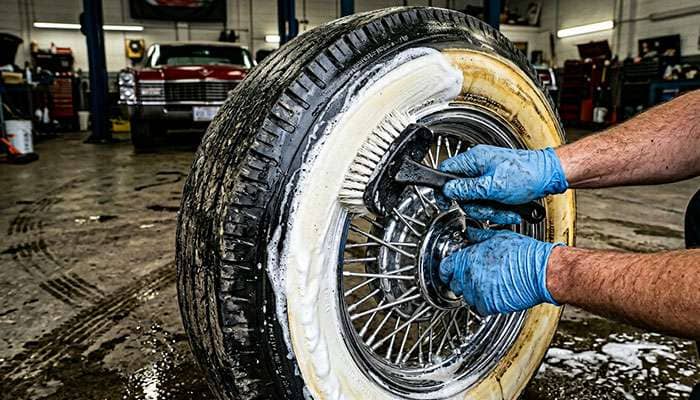 Person scrubbing a yellowed whitewall tire with a stiff nylon brush and whitewall tire cleaner