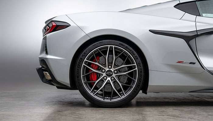 Close-up of a silver Chevrolet sports car focusing on the detailed wheel and tire in a dimly lit garage.