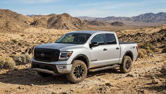 Silver Nissan Titan pickup truck with rugged off-road tires parked in a desert landscape with rocky hills.