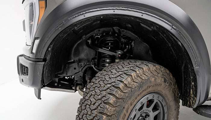 Front wheel well of a full-size pickup truck with the wheel turned to full lock showing the fender liner, pinch weld, and upper control arm behind an oversized tire