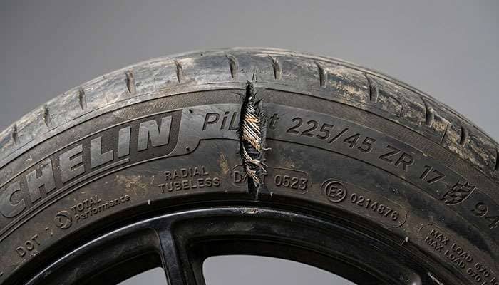 Close-up of a passenger tire sidewall with a visible vertical slash cut, showing exposed cords and air loss