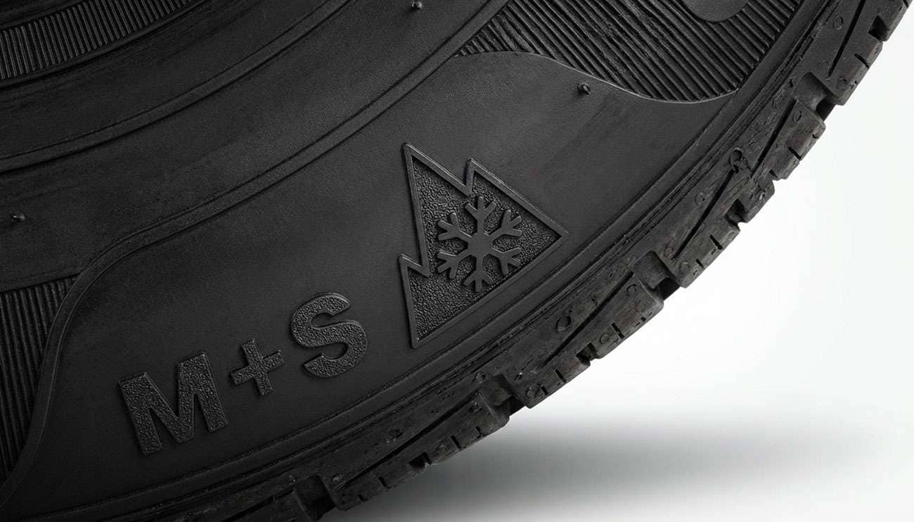 Close-up of tire sidewall showing the Three-Peak Mountain Snowflake (3PMSF) symbol and M+S marking in black and white