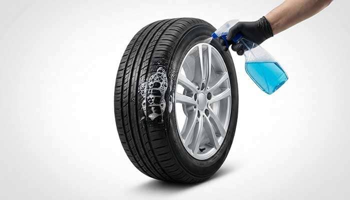 A hand applying soapy water to a car tire to reveal bubbles indicating an air leak.