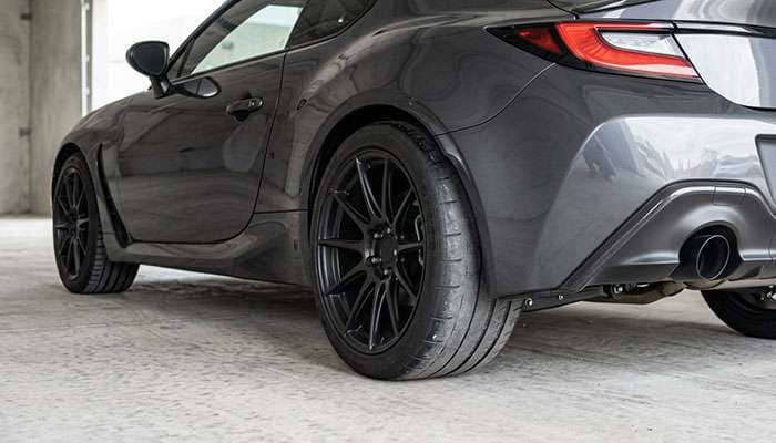Wide rear performance tire on a staggered sports car setup showing worn center tread next to a narrower front tire