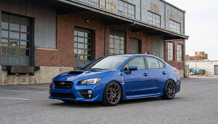 Blue Subaru WRX sedan with aftermarket wheels parked in front of industrial building