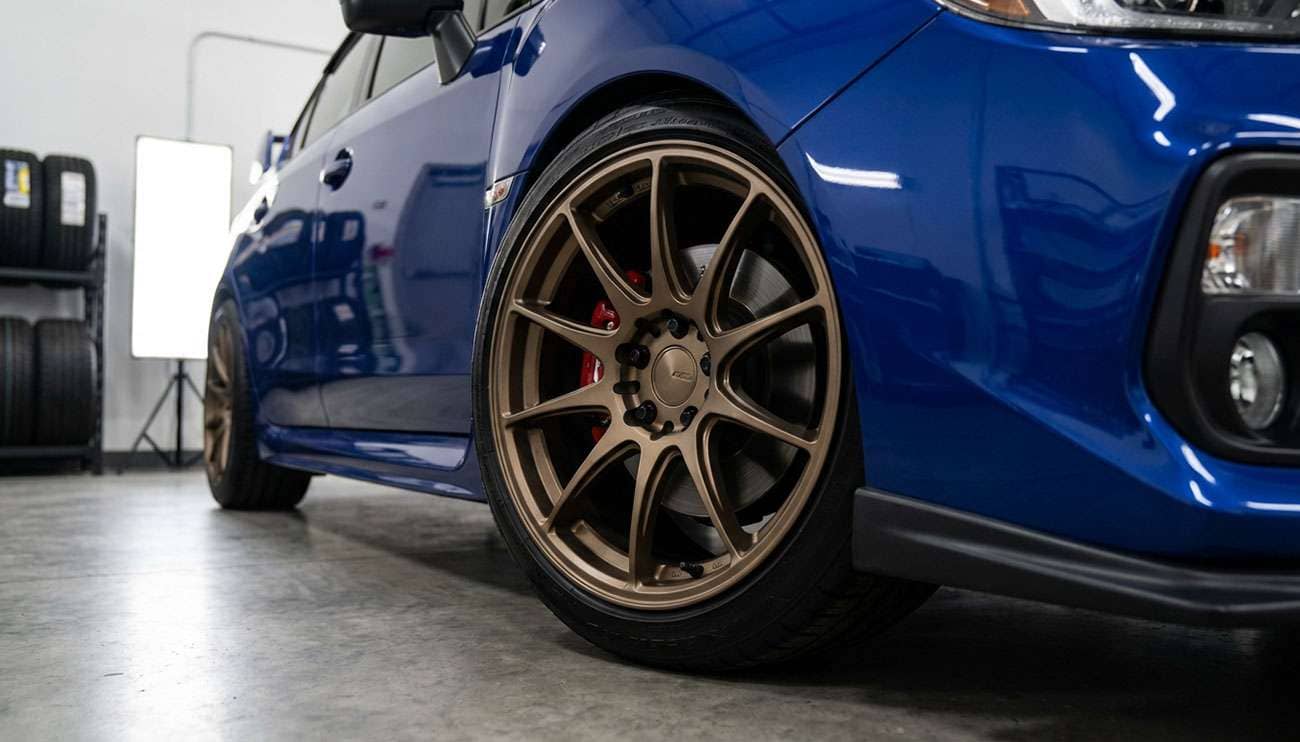 Close-up of aftermarket wheels on a blue Subaru WRX in a well-lit garage setting