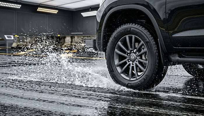 SUV tire being tested on wet pavement showing water spray and braking distance evaluation