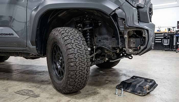 Front wheel well of a 2024 Toyota Tacoma with the bolt-on crash plate removed behind a 35-inch all-terrain tire